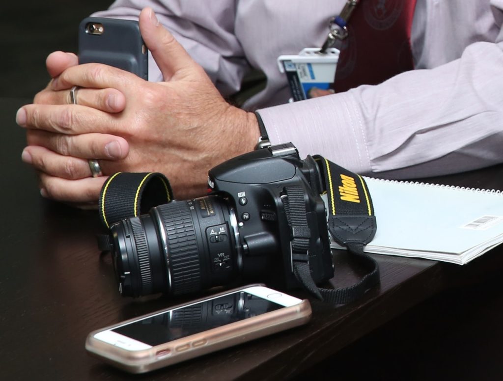 Hands holding phone beside camera and notebook.